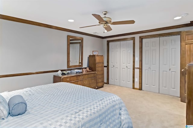 bedroom featuring ornamental molding, a ceiling fan, multiple closets, and light carpet