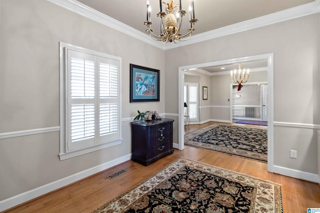 entryway featuring visible vents, a notable chandelier, wood finished floors, crown molding, and baseboards