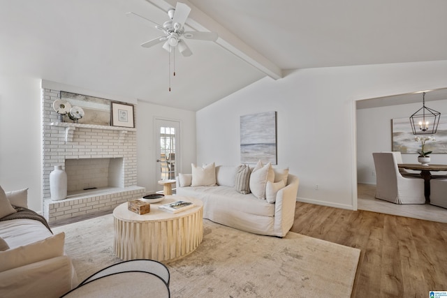 living room featuring a fireplace, lofted ceiling with beams, wood finished floors, baseboards, and ceiling fan with notable chandelier