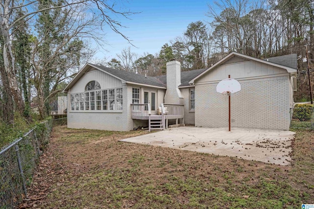 rear view of house featuring a fenced backyard, a chimney, a deck, and brick siding