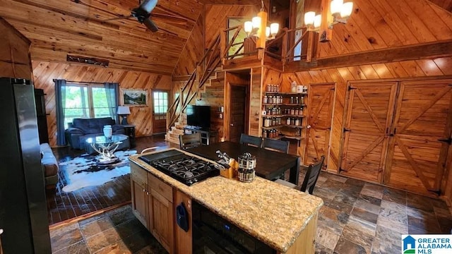 kitchen with stone tile flooring, wood ceiling, wooden walls, black gas stovetop, and high vaulted ceiling