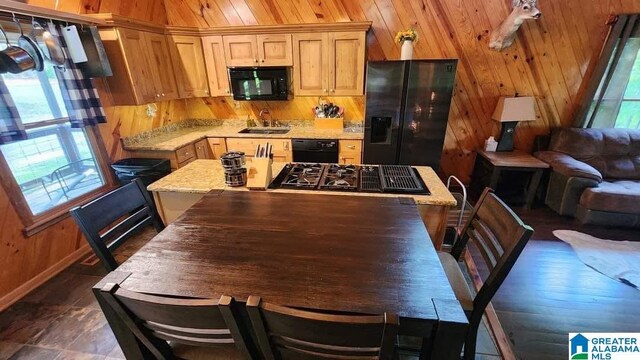 kitchen featuring a center island, open floor plan, a sink, wooden walls, and black appliances