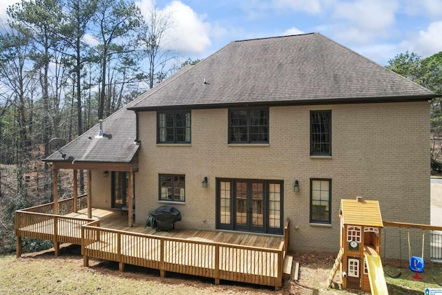 back of house with a shingled roof, french doors, a wooden deck, a playground, and brick siding