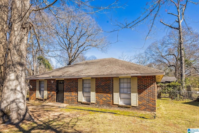 view of front of house with a shingled roof, fence, a front lawn, and brick siding