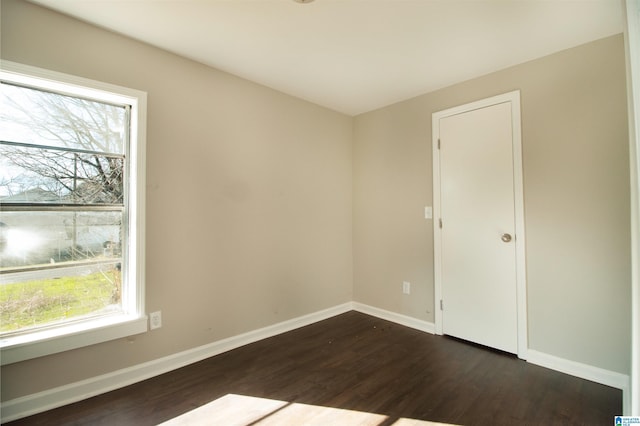 empty room featuring dark wood-style floors, plenty of natural light, and baseboards