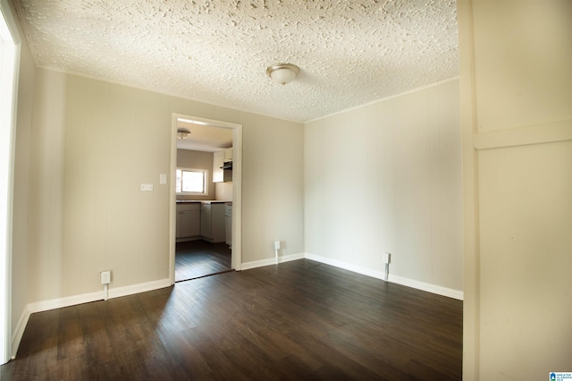 spare room with a textured ceiling, dark wood-style flooring, and baseboards