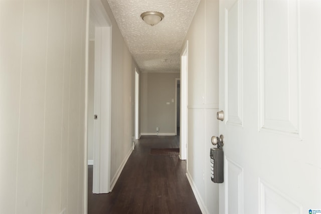 hallway featuring a textured ceiling, dark wood-style flooring, and baseboards