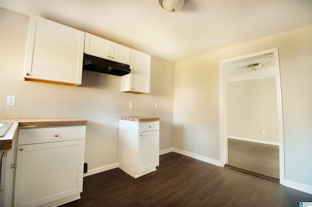 kitchen with under cabinet range hood, baseboards, white cabinets, and dark wood-type flooring