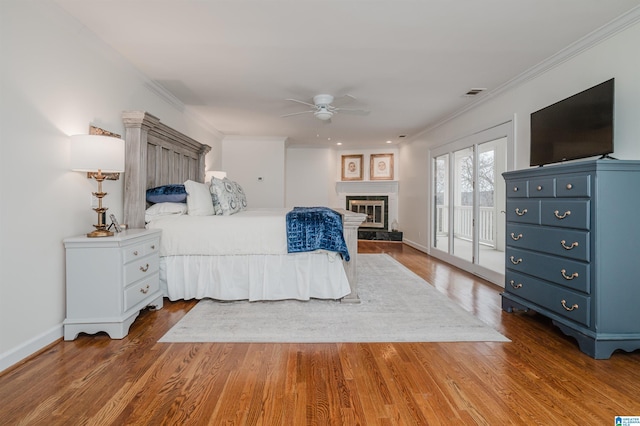 bedroom with visible vents, a glass covered fireplace, wood finished floors, access to exterior, and crown molding