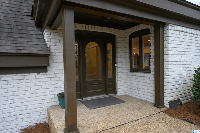 view of exterior entry featuring brick siding and roof with shingles