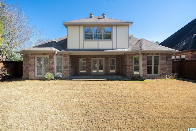 rear view of property featuring brick siding, fence, french doors, a lawn, and roof with shingles