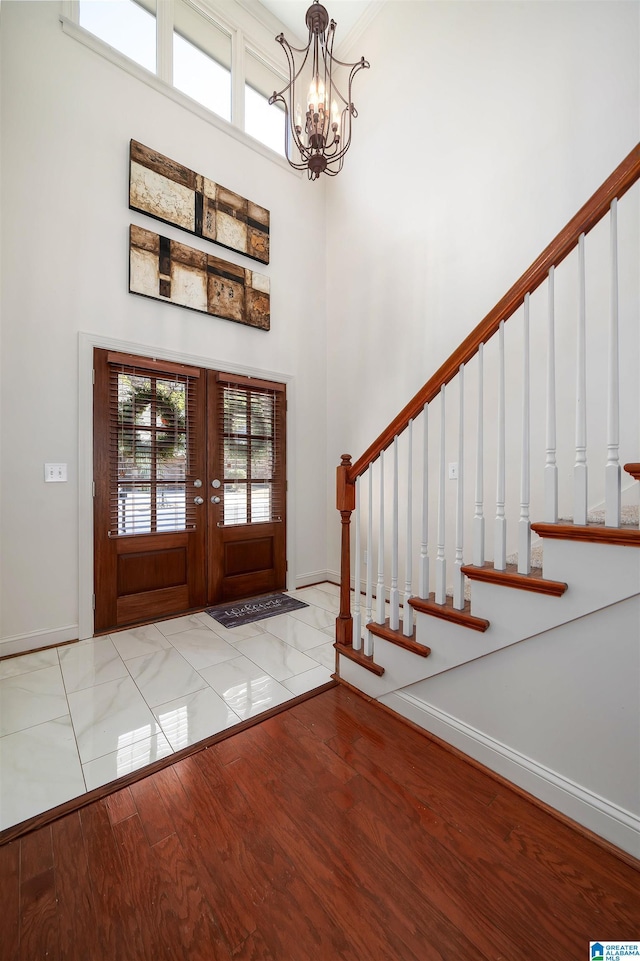 entryway featuring wood finished floors, a towering ceiling, stairs, french doors, and an inviting chandelier