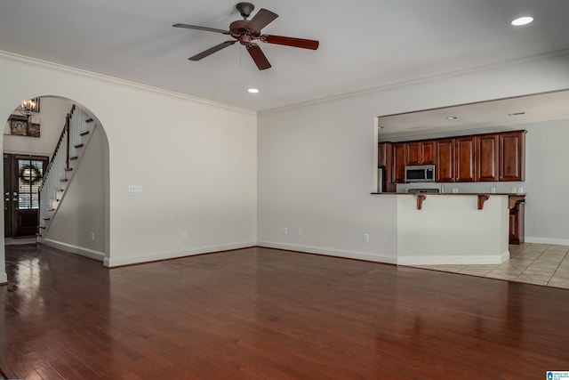 unfurnished living room featuring arched walkways, wood finished floors, baseboards, stairs, and crown molding