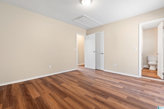 unfurnished bedroom featuring ensuite bath, wood finished floors, attic access, and baseboards