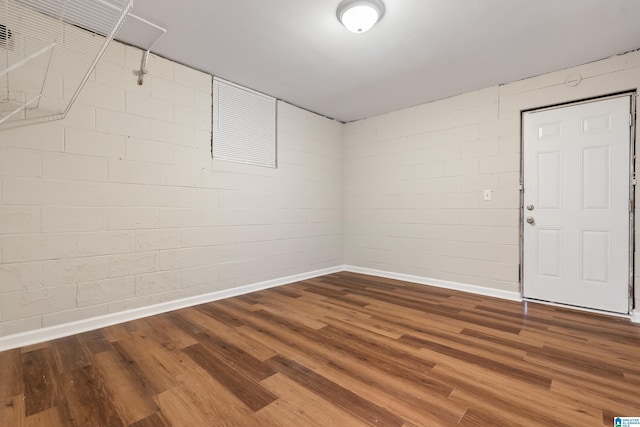 unfurnished room with wood finished floors, concrete block wall, and baseboards