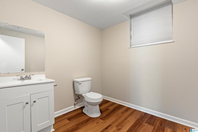 half bathroom with vanity, wood finished floors, toilet, and baseboards