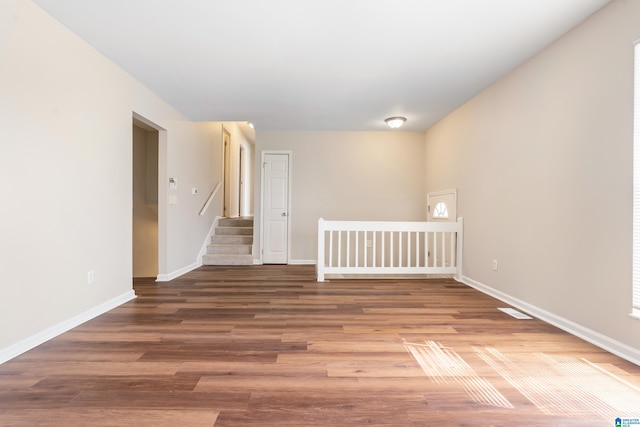 spare room featuring stairs, wood finished floors, visible vents, and baseboards