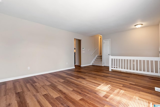 empty room with stairs, baseboards, and wood finished floors