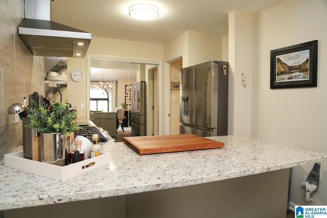 kitchen featuring light stone countertops, wall chimney exhaust hood, stainless steel fridge with ice dispenser, and freestanding refrigerator