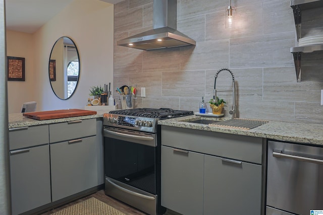 kitchen with gray cabinets, a sink, appliances with stainless steel finishes, exhaust hood, and tasteful backsplash