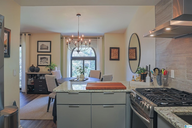 kitchen with light stone counters, dark wood finished floors, stainless steel gas stove, wall chimney exhaust hood, and tasteful backsplash