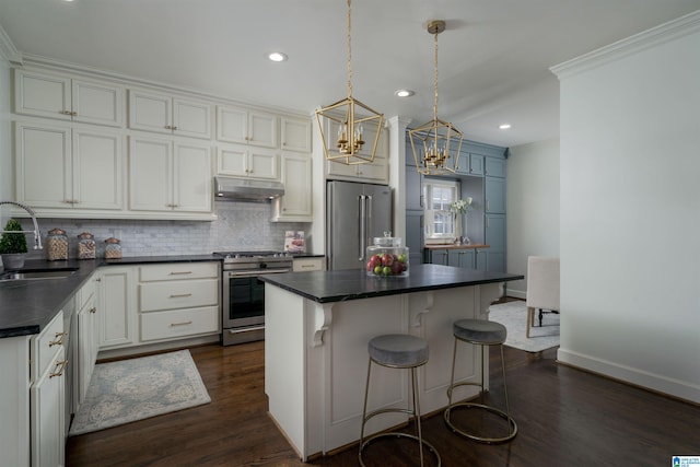 kitchen with a sink, decorative backsplash, under cabinet range hood, appliances with stainless steel finishes, and dark countertops