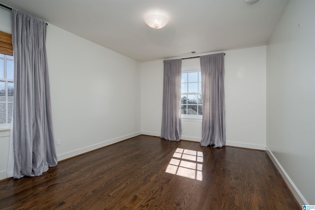 spare room featuring dark wood finished floors, visible vents, and baseboards