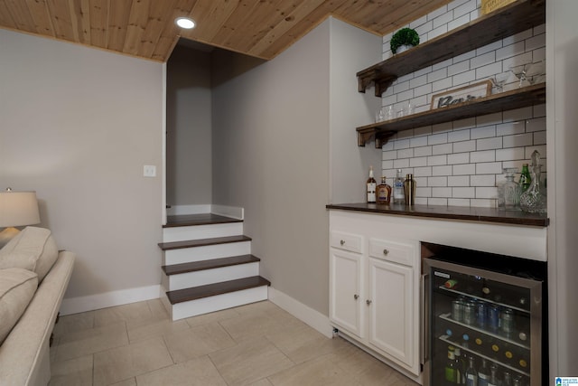 bar featuring backsplash, wine cooler, a bar, wooden ceiling, and baseboards