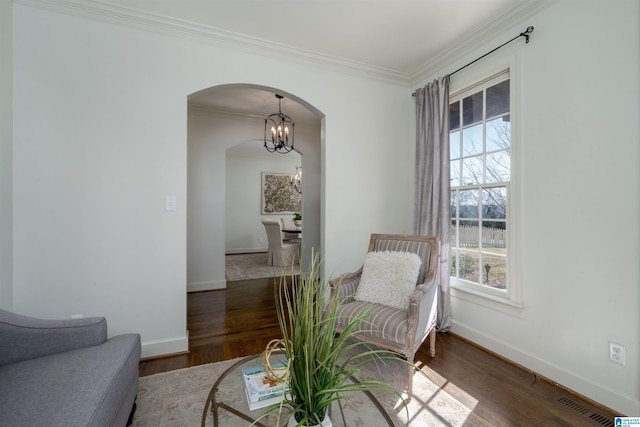 sitting room with crown molding, wood finished floors, arched walkways, and baseboards