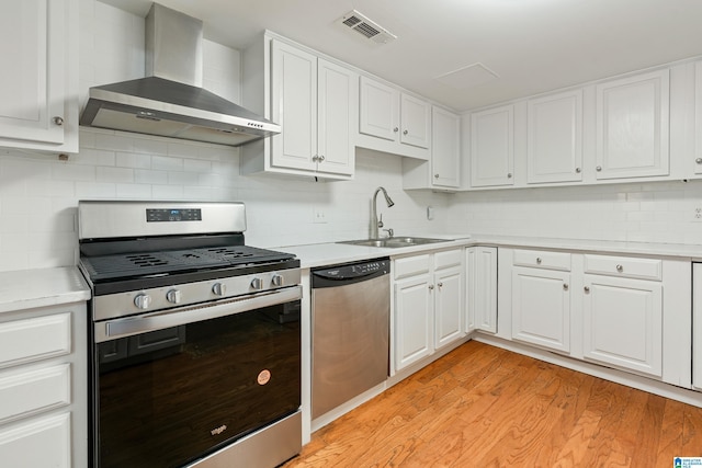 kitchen with light wood finished floors, visible vents, appliances with stainless steel finishes, wall chimney exhaust hood, and a sink