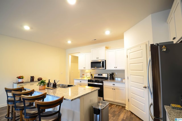 kitchen featuring light stone countertops, white cabinets, appliances with stainless steel finishes, a center island, and dark wood-style floors