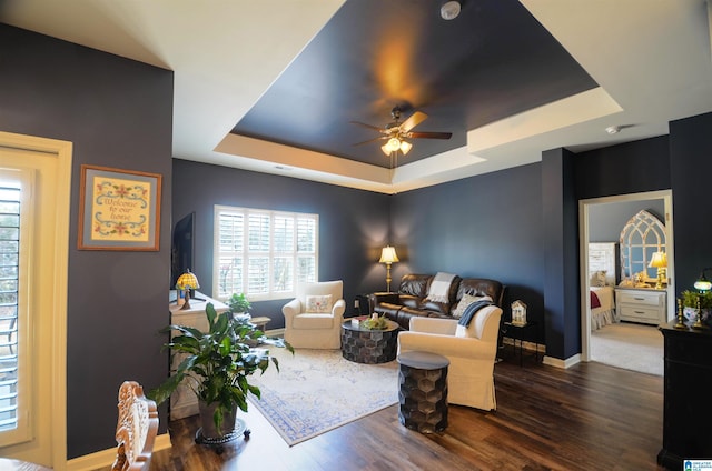 living area with a tray ceiling, dark wood-style flooring, ceiling fan, and baseboards