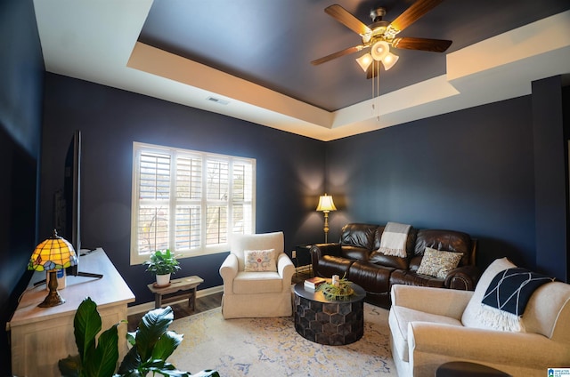 living room with a ceiling fan, a tray ceiling, visible vents, and wood finished floors