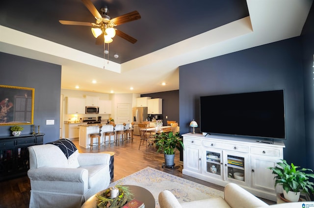 living area featuring a tray ceiling, ceiling fan, recessed lighting, and wood finished floors