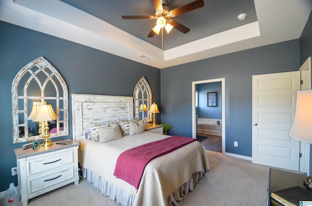 bedroom with ensuite bathroom, light colored carpet, visible vents, baseboards, and a raised ceiling