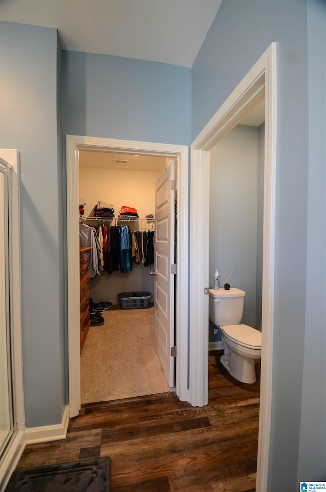 full bathroom featuring toilet, a shower stall, a walk in closet, and wood finished floors