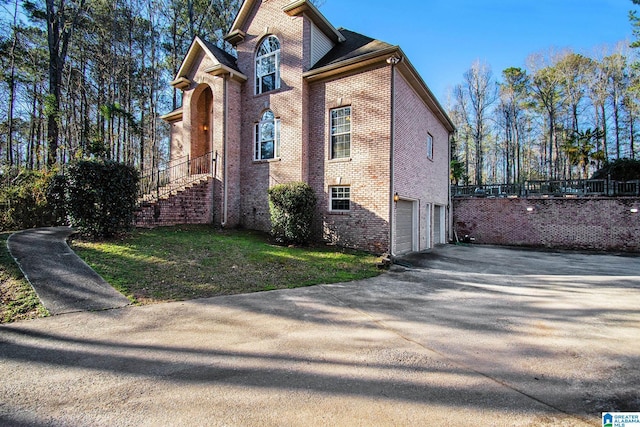 view of property exterior featuring an attached garage, brick siding, driveway, and a yard