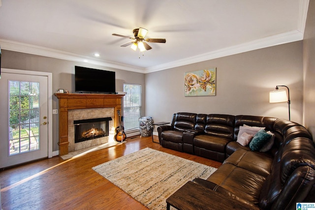 living area featuring a high end fireplace, baseboards, ornamental molding, wood finished floors, and a ceiling fan