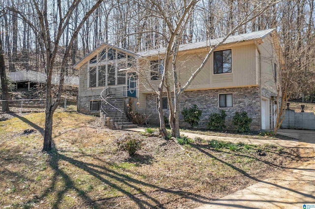 view of front facade featuring metal roof, an attached garage, brick siding, fence, and stairs