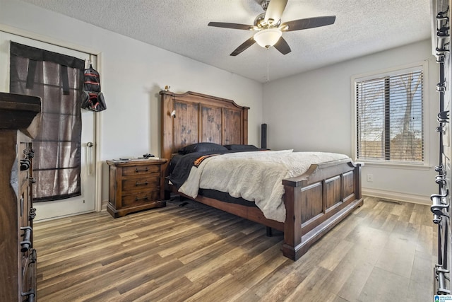 bedroom with ceiling fan, a textured ceiling, baseboards, and wood finished floors