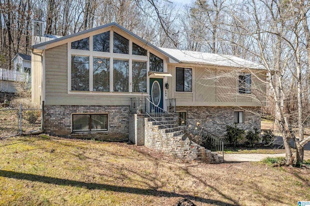 raised ranch featuring fence, a front lawn, and brick siding