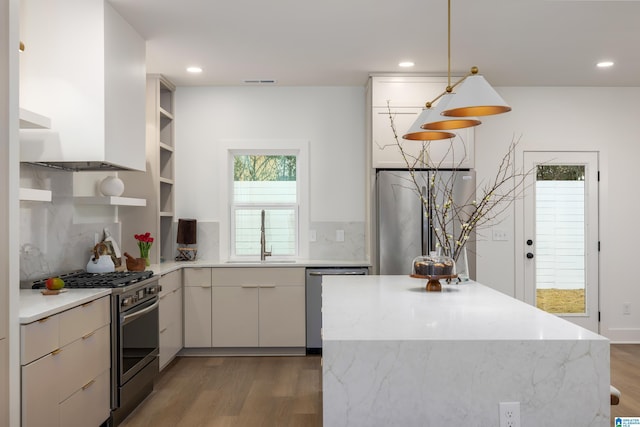 kitchen with a sink, open shelves, light wood-style floors, appliances with stainless steel finishes, and decorative backsplash