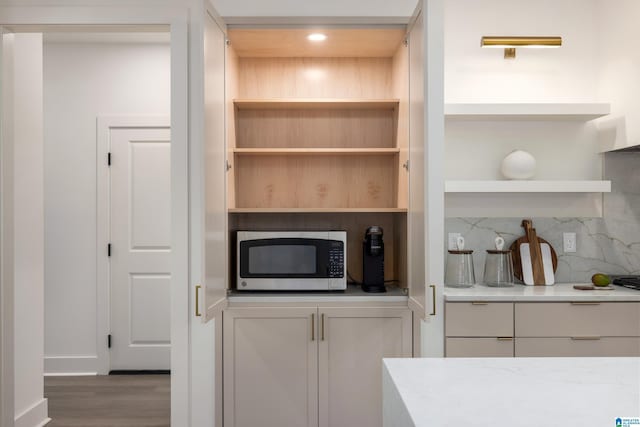 kitchen with open shelves, stainless steel microwave, wood finished floors, white cabinetry, and decorative backsplash