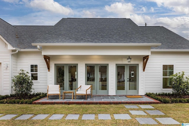 entrance to property with a patio, a yard, french doors, and roof with shingles