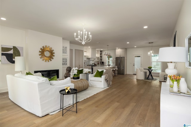 living room featuring light wood finished floors, a notable chandelier, recessed lighting, and a glass covered fireplace