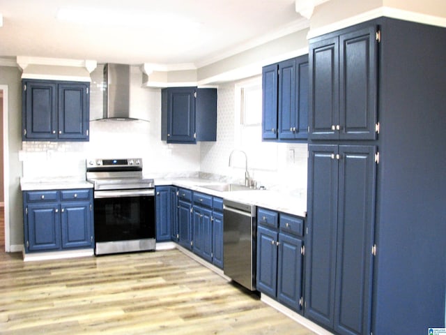 kitchen with crown molding, wall chimney range hood, blue cabinets, a sink, and stainless steel appliances