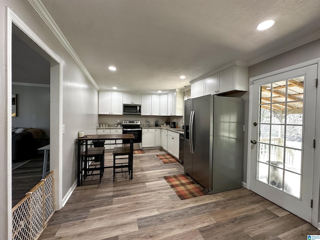 kitchen featuring appliances with stainless steel finishes, ornamental molding, wood finished floors, white cabinetry, and recessed lighting