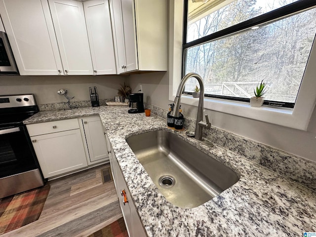 kitchen with wood finished floors, a sink, white cabinets, stainless steel range with electric cooktop, and light stone countertops