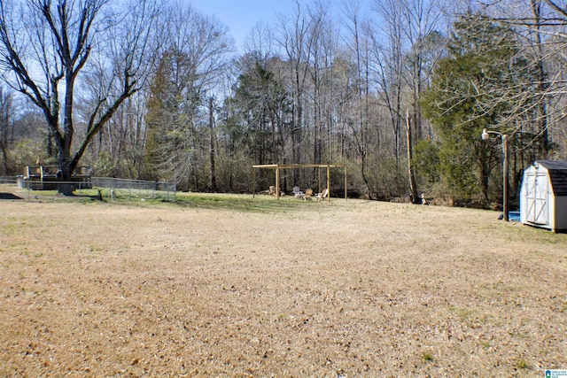 view of yard featuring a shed, fence, a view of trees, and an outbuilding