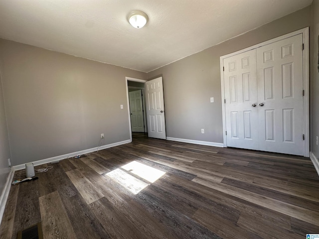 unfurnished bedroom with dark wood-style floors, a closet, visible vents, and baseboards